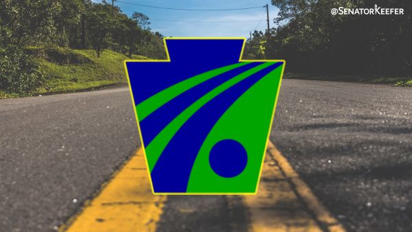 Photo of black top road with a yellow line down the center and the PA state keystone symbol centered in the middle in blue and green.