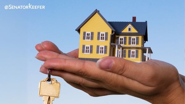 Blue sky with a hand holding a two-story yellow house and a set of keys hanging from the finger.