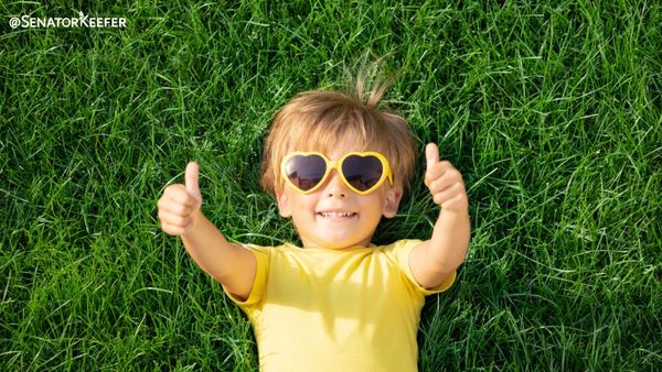 Kid laying in the grass with yellow heart sunglasses on and giving two thumbs up.