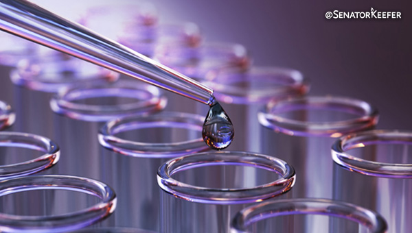 A dropper with a bead of water hanging over a glass beaker.