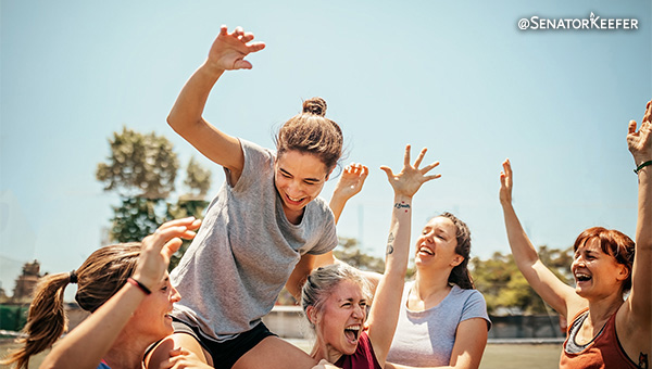Women’s sports team cheering with one woman being held up on shoulders.