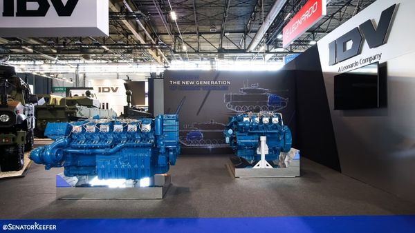 An exhibition booth featuring two large blue industrial engines on display, with a backdrop showing a vehicle outline and the IDV (A Leonardo Company) branding.