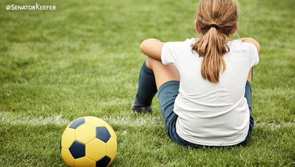 a girl sitting on a soccer field with ball.