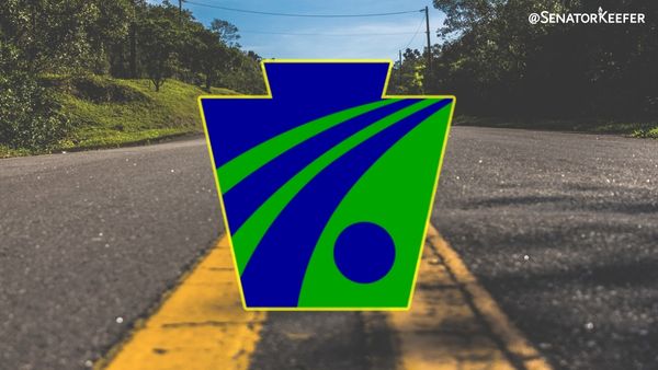 black top road with a yellow line down the center and the PA state keystone symbol centered in the middle in blue and green.