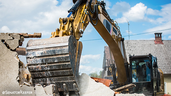 a backhoe knocking down a concrete wall.