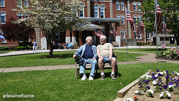Two senior citizens sitting on a bench in a garden.