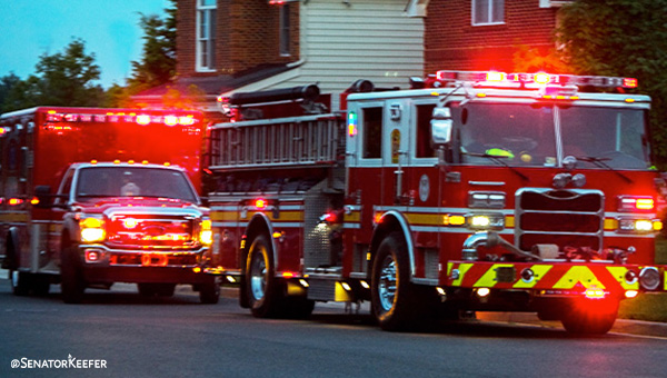 Two emergency vehicles—a fire truck and an ambulance—parked on a residential street with their red lights flashing.