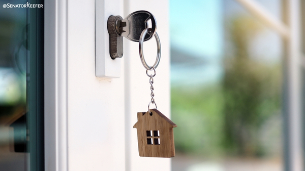 Close-up of a key inserted into a door lock, with a wooden house-shaped keychain hanging from the key.