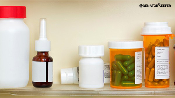 Various medication containers on a shelf, including prescription pill bottles, a small spray bottle, and other unlabeled plastic containers, arranged against a light-colored wall.